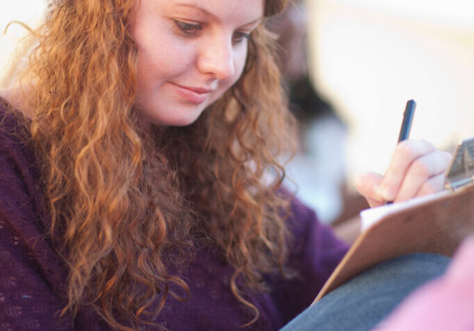 Young woman wearing knit hat writing on clipboard